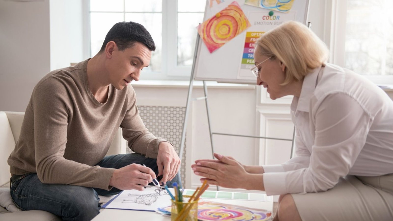 a man drawing while a woman is talking to the man, showing art therapy