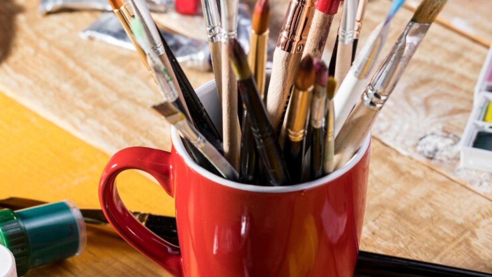 assortment of paint brushes in mug with palette